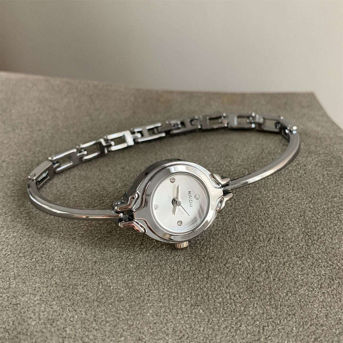A silver-tone bangle watch with a round white dial and a small visible 'MOON' brand mark, resting on a textured gray surface.