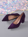 A pair of deep purple velvet pointed-toe pumps with block heels, displayed on a gray surface with a shimmering, iridescent sequin fabric in the background.