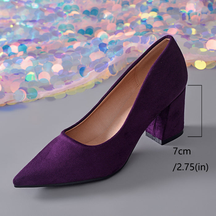 A single purple velvet pointed-toe pump with a chunky block heel, shown on a gray surface with a decorative iridescent sequin backdrop and a height marker indicating 7 cm (2.75 in).