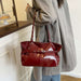 A person wearing an oversized light gray coat holds a shiny deep red tote bag with silver-tone hardware in an indoor room setting.