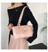 A woman wearing a black off-the-shoulder long-sleeve top and a light pink pleated skirt carries a shiny metallic pink shoulder bag with a wide strap and silver studs.