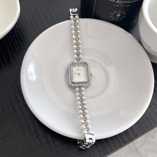 Silver watch with pearl bracelet on a white plate