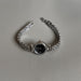 A silver-tone metal bracelet watch with a round black dial, photographed on a light gray textured surface.