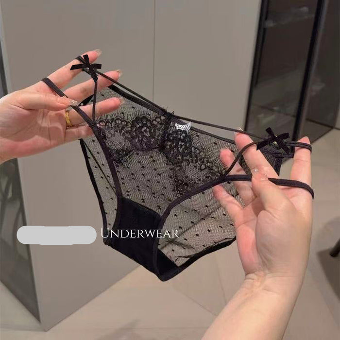 Black lace and mesh panties with bow details on the straps, held up by two hands against an indoor background. 