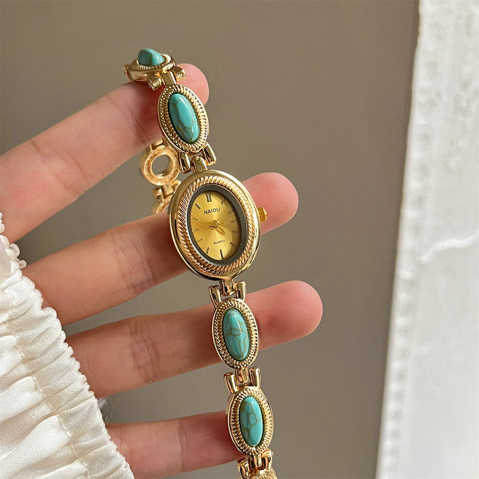 Gold watch with turquoise stones held by a hand against a neutral background