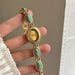Gold watch with turquoise stones held by a hand against a neutral background