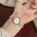 Gold watch with pearl bracelet on a wrist against a blurred background