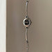 A silver-tone metal link watch with a round black dial and small crystal hour markers, hanging against a plain beige wall.