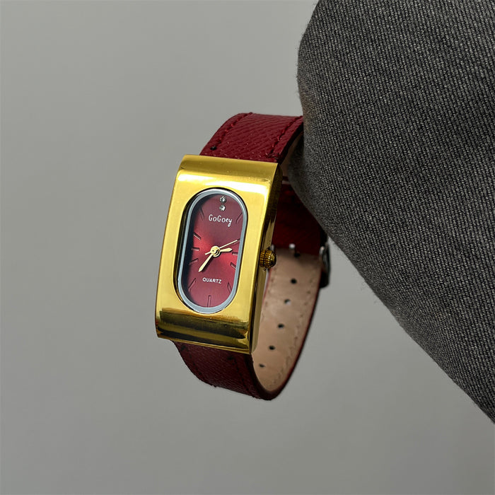 Gold watch with red face and leather strap held by a gray sleeve.