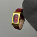 Gold watch with red face and leather strap held by a gray sleeve.
