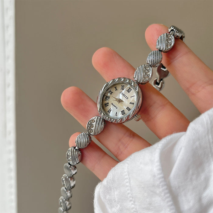 Silver watch with a bracelet held in a hand against a neutral background