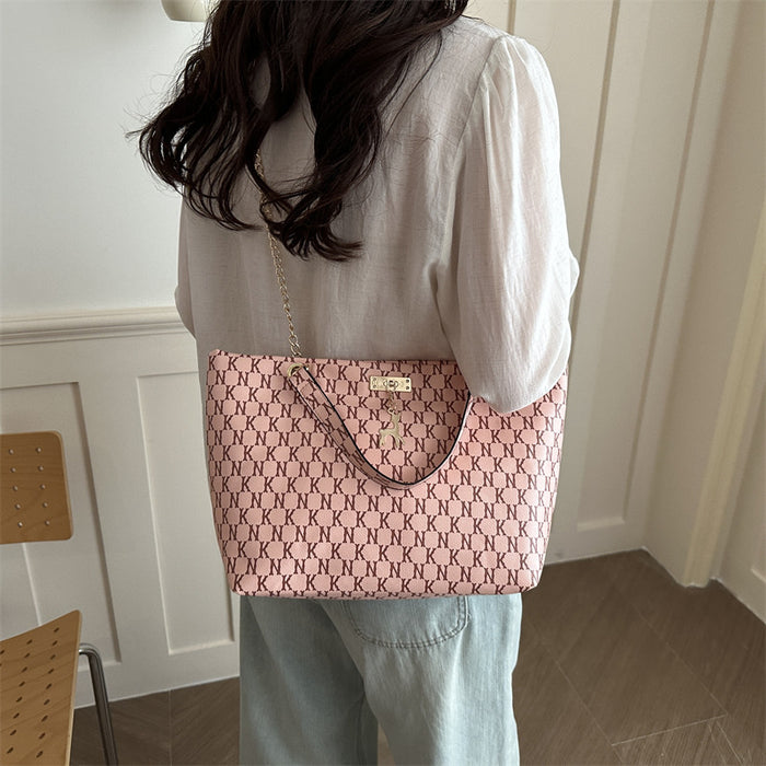 A woman viewed from behind wearing a light pink and beige patterned tote bag with a gold chain strap, styled with a white blouse and light blue jeans in an indoor setting.
