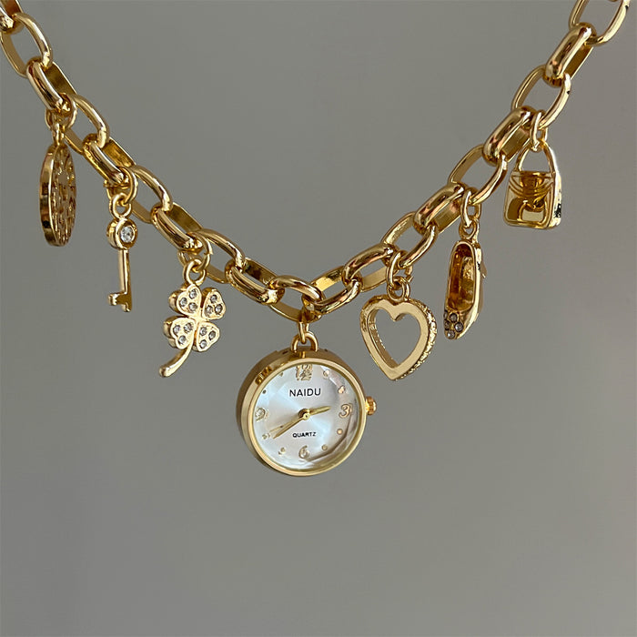Gold charm bracelet with a watch and various charms on a gray background