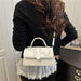 A woman wearing a black long-sleeve top and a white pleated ruffled skirt carries a small white top-handle handbag over her shoulder in an indoor setting.