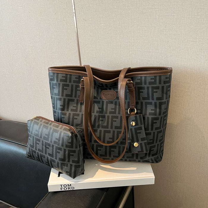 A Fendi tote bag in dark gray and black FF monogram canvas with brown leather trim, displayed on a white book with a matching small pouch beside it.