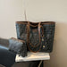 A Fendi tote bag in dark gray and black FF monogram canvas with brown leather trim, displayed on a white book with a matching small pouch beside it.