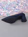 A single navy blue velvet pointed-toe heeled boot shown from a side angle, with a black textured outsole and block heel, set against a gray background with a shimmering sequin fabric backdrop.