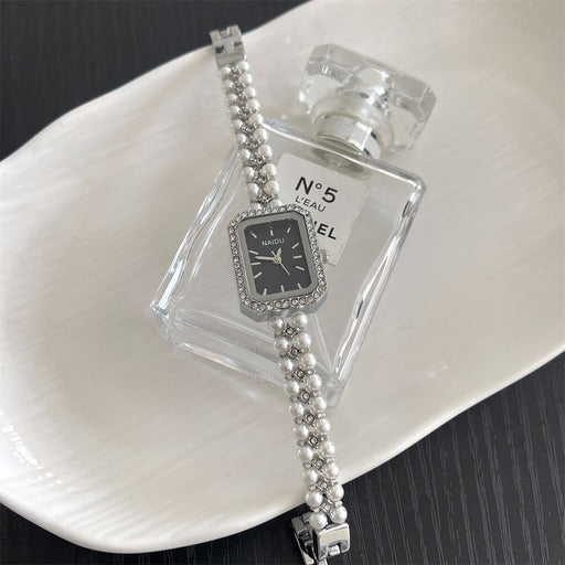 Silver watch with pearl bracelet on a white plate with a Chanel perfume bottle.