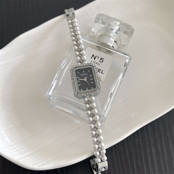 Silver watch with pearl bracelet on a white plate with a Chanel perfume bottle.
