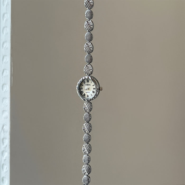 Silver bracelet with a watch face on a plain background