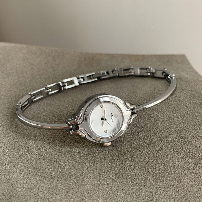 A silver-tone bangle watch with a round white dial and a small visible 'MOON' brand mark, resting on a textured gray surface.