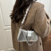 A woman wearing a brown herringbone coat carries a metallic silver shoulder bag with a studded strap and chain detail.