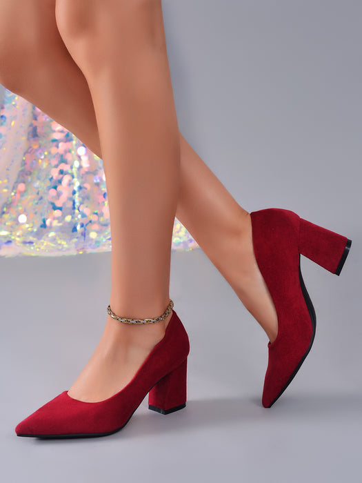A pair of red suede block-heel pumps with ankle straps, shown on a model's feet against a gray studio background.
