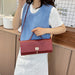 A woman wearing a white t-shirt and white skirt carries a textured red handbag with a top handle and shoulder strap, styled with a light blue knit vest in a kitchen setting.