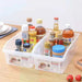 Two clear plastic kitchen organizer bins filled with assorted condiments, spices, and stock bottles on a light wood tabletop.