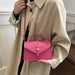 A person wearing a beige trench coat carries a bright pink structured handbag with a top handle, shoulder strap, and front flap closure with a decorative clasp.