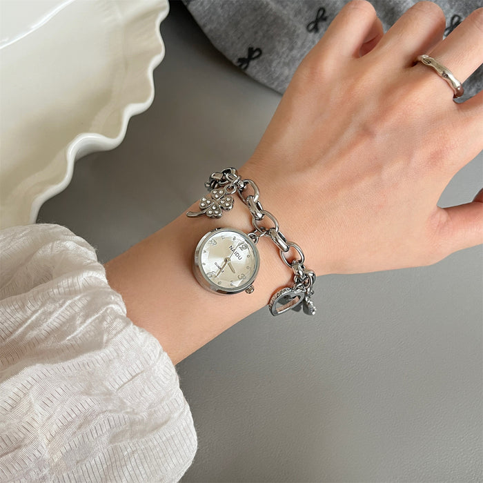 Hand wearing a silver watch with charm bracelet on a neutral background