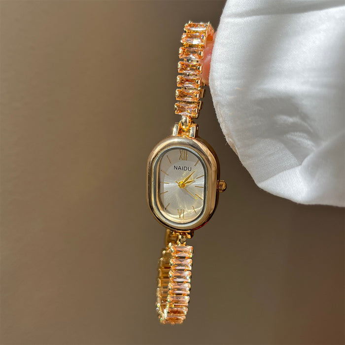 Gold wristwatch with gemstone accents held by a hand against a neutral background