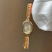 Gold wristwatch with gemstone accents held by a hand against a neutral background