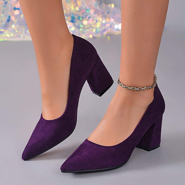 A pair of women's pointed-toe high heels in deep purple suede, shown on a model's feet against a neutral gray background with a sparkly bokeh backdrop.