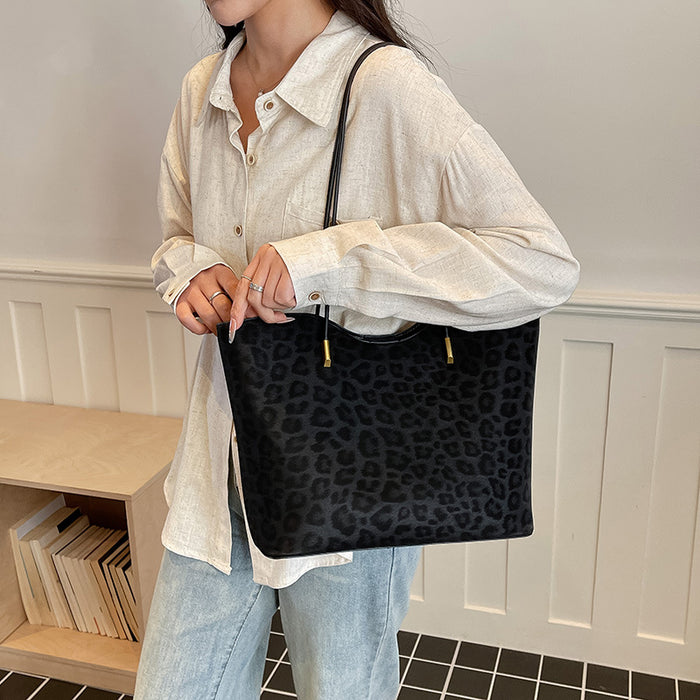 A person wearing a cream linen shirt and light blue jeans carries a large black leopard-print tote bag with gold-tone hardware in an indoor setting.