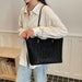 A person wearing a cream linen shirt and light blue jeans carries a large black leopard-print tote bag with gold-tone hardware in an indoor setting.