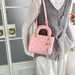 A person wearing a gray pleated vest over a white long-sleeve top carries a pink quilted top-handle handbag with gold-tone hardware and a pearl tassel charm, standing indoors near a glass-paneled door.