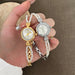 Two pearl-wrapped watches held in a hand against a brown background