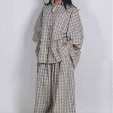 A person wearing a loose, two-piece plaid outfit in light beige and gray tones, photographed against a plain light gray background.