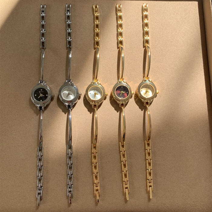 Five women's analog wristwatches with decorative links are lined up on a beige textured surface. Three watches are silver-toned and two are gold-toned, with black, white, and mother-of-pearl dials.