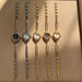 Five women's analog wristwatches with decorative links are lined up on a beige textured surface. Three watches are silver-toned and two are gold-toned, with black, white, and mother-of-pearl dials.