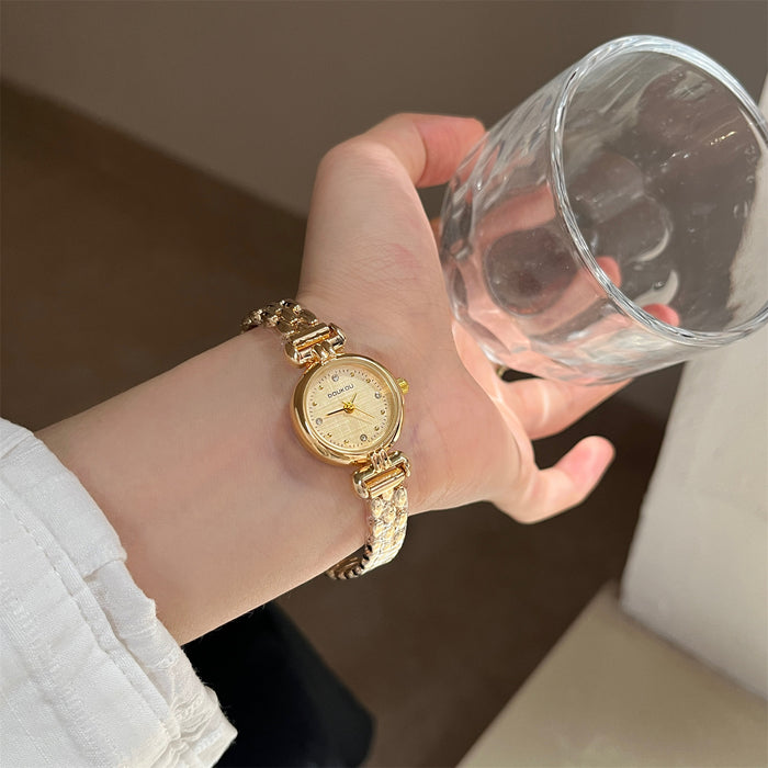 Hand wearing a gold watch holding a clear glass against a neutral background