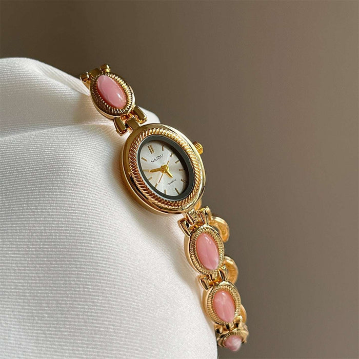 Gold watch with pink gemstones on a white cushion