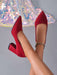 A pair of red suede pointed-toe pumps with block heels, shown on a model's feet against a gray background with a sequined chandelier decoration.