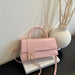A pink faux leather handbag with a gold FF logo clasp, resting on a white book next to a white vase with dried branches.