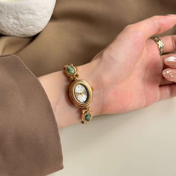 Gold watch with green gemstones on a wrist against a neutral background