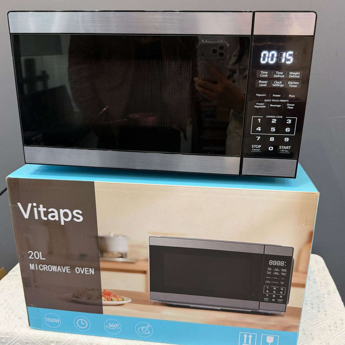 A Vitaps 20L microwave oven with a stainless steel and black glass door, shown resting on top of its blue and brown retail packaging box.