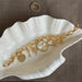 Gold bracelet with charms on a white shell dish on a brown surface