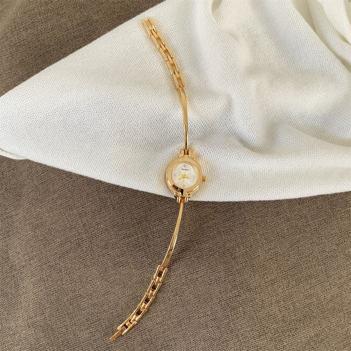 A gold-tone watch with a slim round dial and matching chain bracelet, styled on a white fabric surface over a brown textured background.