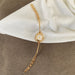 A gold-tone watch with a slim round dial and matching chain bracelet, styled on a white fabric surface over a brown textured background.
